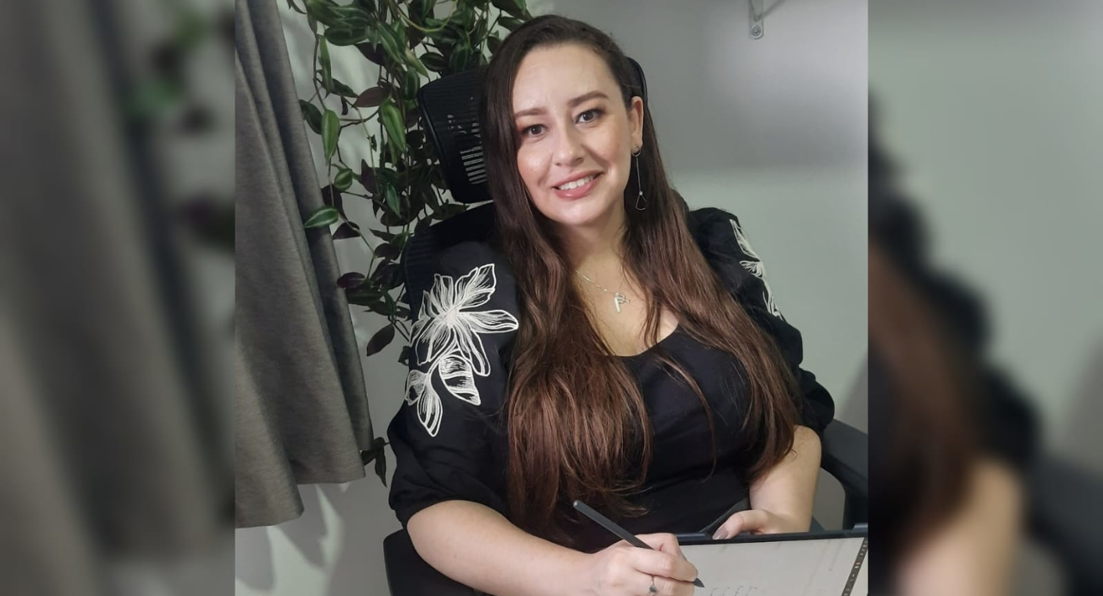 Psicóloga Fernanda olhando para camera sorrindo, com planta ao fundo